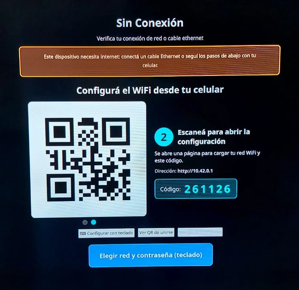 Foto del mismo televisor mostrando el paso 2: el código QR que abre la página de configuración en el celular, la dirección 10.42.0.1 y el código de seis dígitos